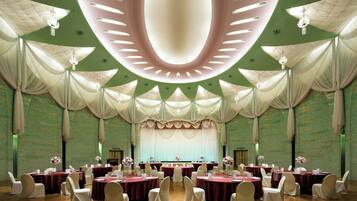 A banquet hall with round tables, white chairs, and a stage with draped curtains.