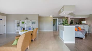 A spacious living area with a sofa, a dining table with chairs, a white console table with plants, and a patterned rug.