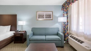 A hotel room with a bed, a sofa, a bedside table with a lamp, a framed picture on the wall, and a window with curtains. - Quality Inn Clute Freeport (Clute)