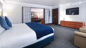 A hotel room with a large bed, a TV mounted on the wall, a wooden dresser, and a desk with a chair.