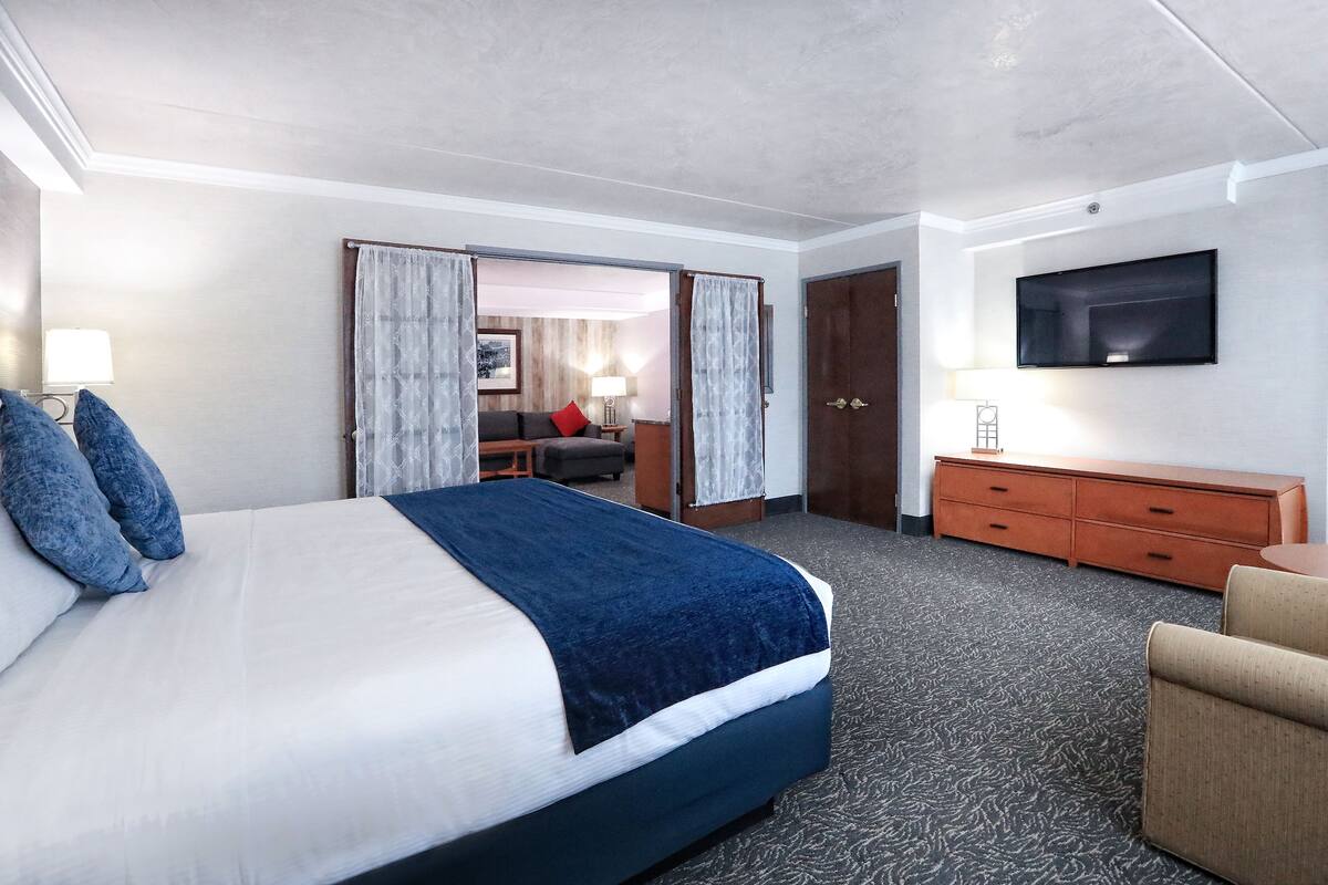 A hotel room with a large bed, a TV mounted on the wall, a wooden dresser, and a desk with a chair.