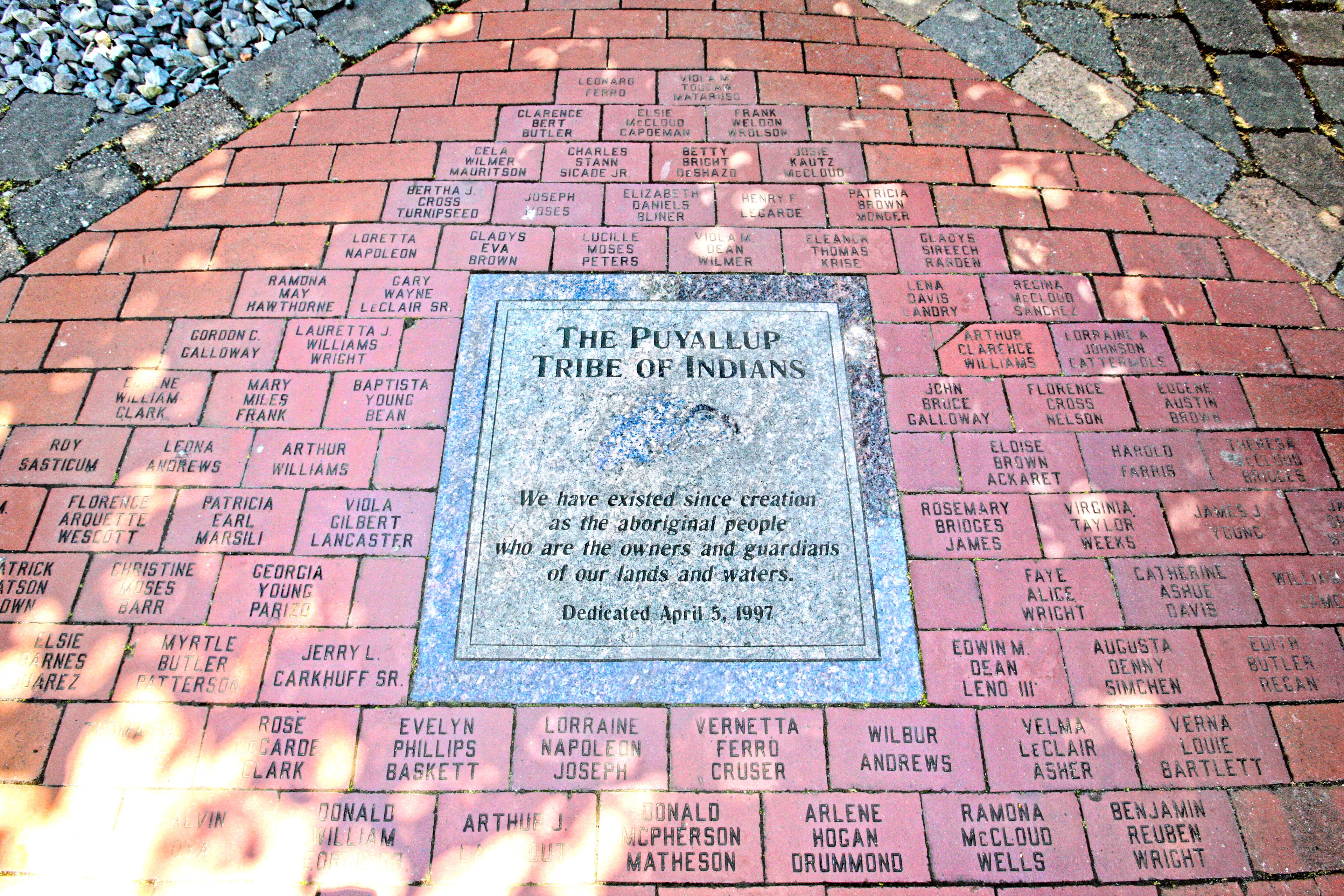 A commemorative plaque on a brick pavement with names inscribed.