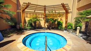 A circular pool with a tiled edge, surrounded by a pergola structure, and various plants.