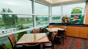 A restaurant with large windows offering a view of a highway and greenery. Tables are set with chairs, and a counter is visible with a sign.