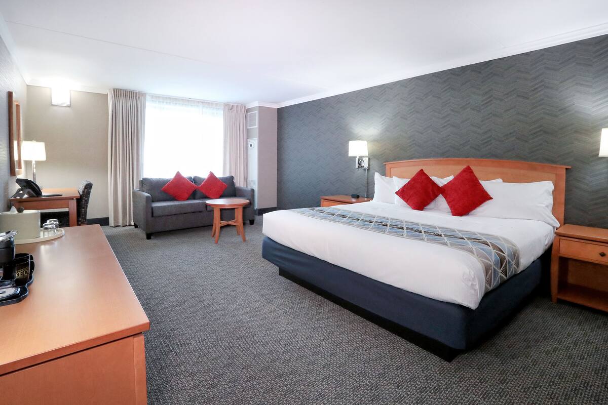 A hotel room with a large bed, a desk with a phone, a chair, and a small table.