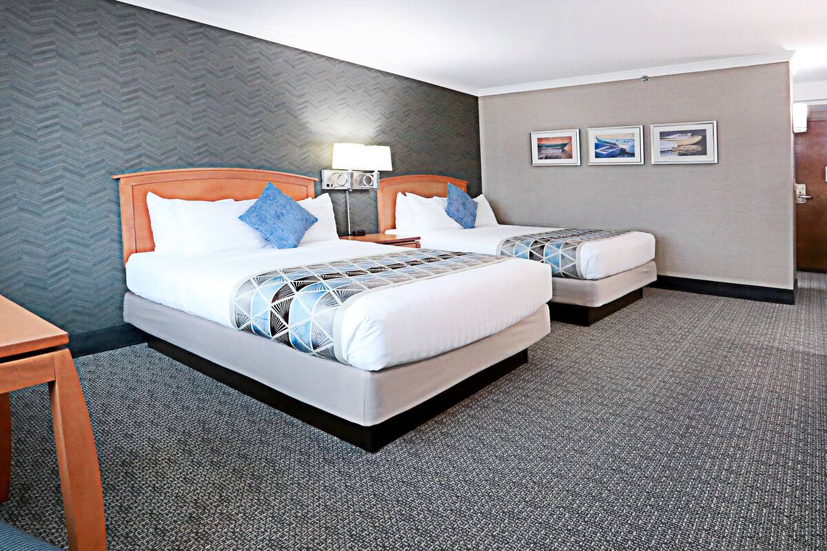 A hotel room with two beds, a desk, and a lamp.