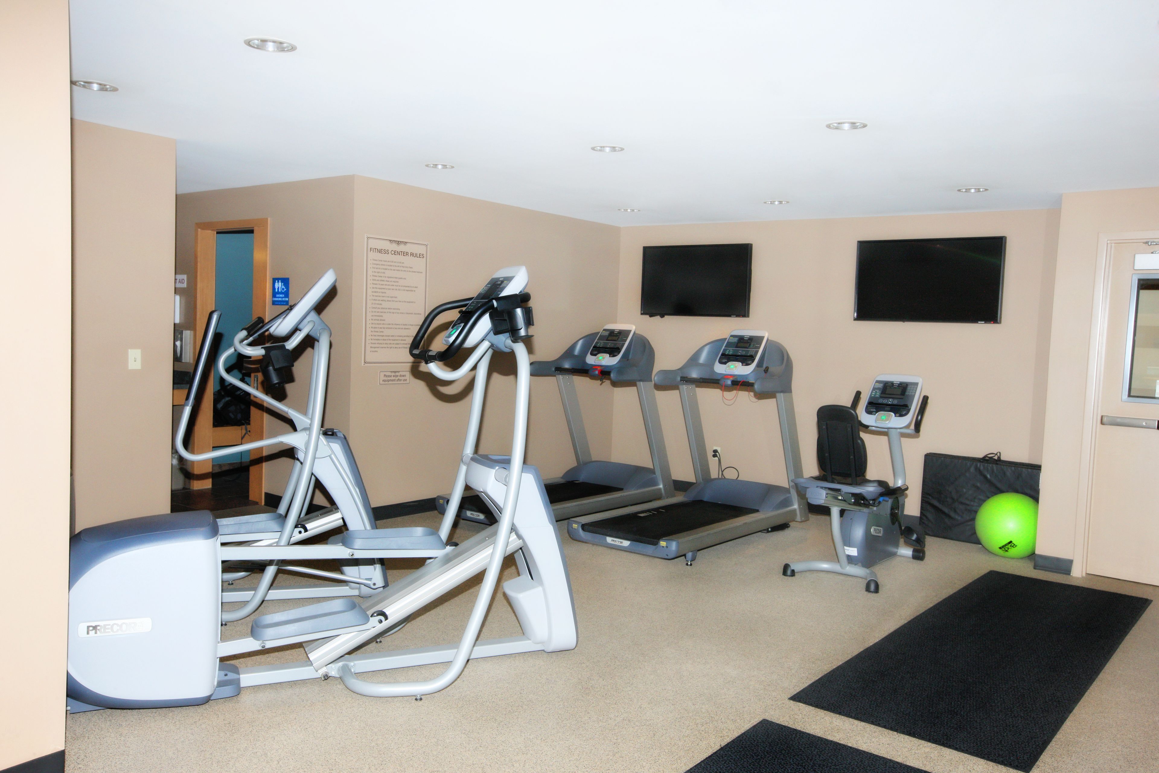 A fitness room with treadmills, an elliptical, a stationary bike, and a green exercise ball.