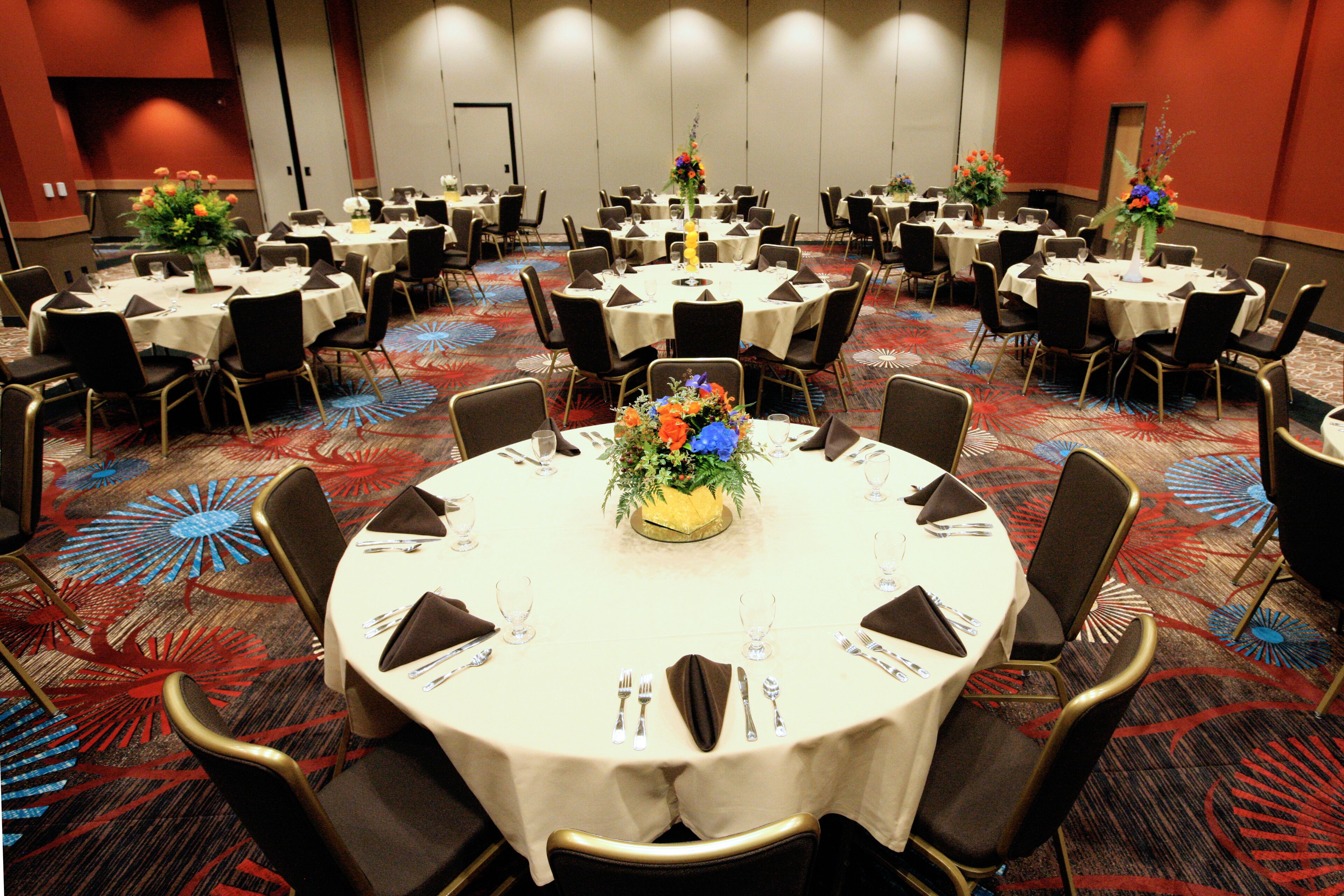 A conference room with multiple round tables, each set with chairs, place settings, and floral centerpieces.