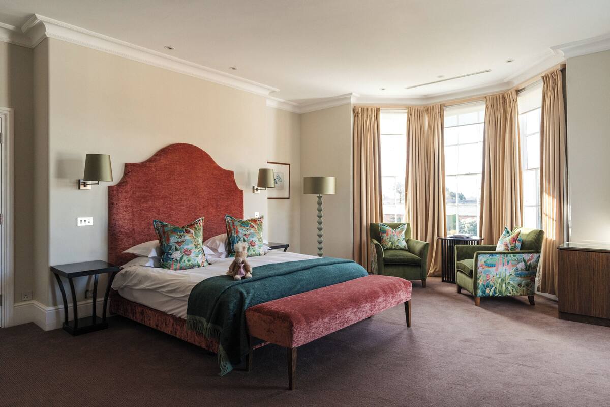 Een slaapkamer met een groot bed, twee stoelen, een klein tafeltje en een bank.