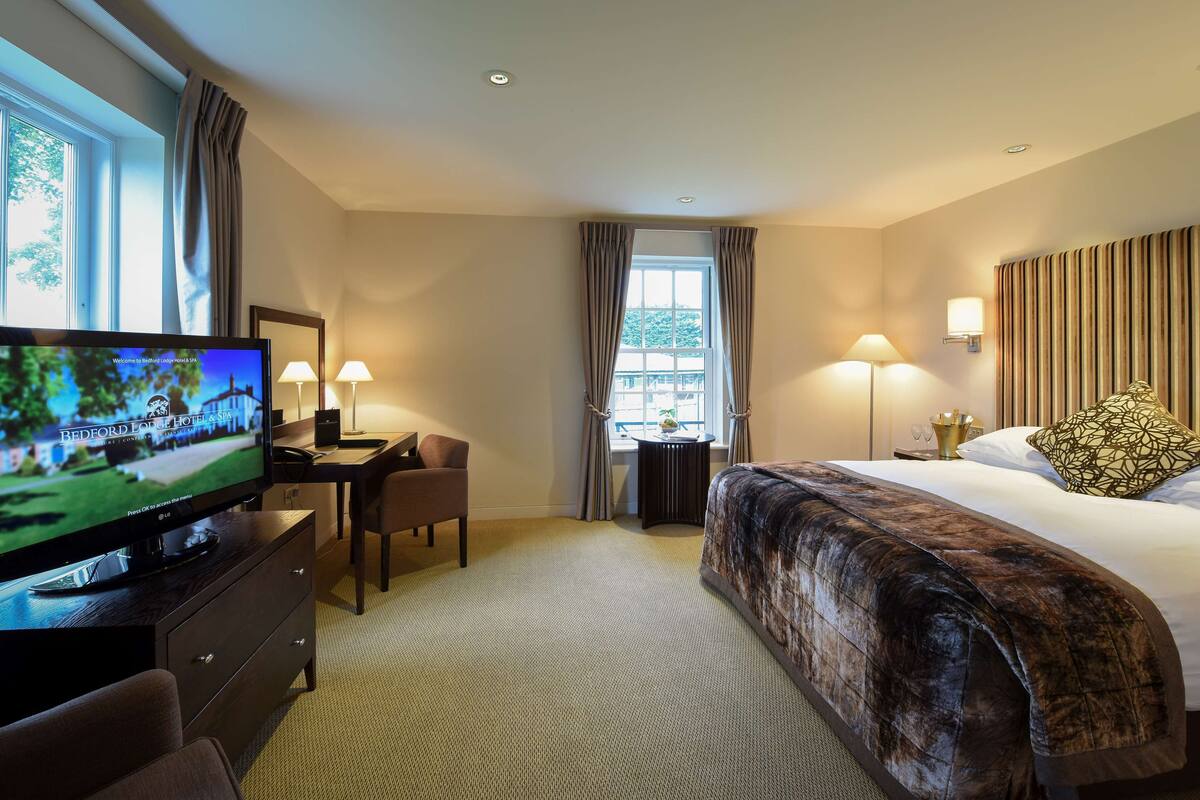 Een hotelkamer met een bed, een bureau met een computer, een televisie en een raam met gordijnen.