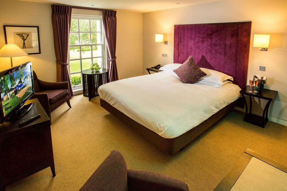 Een hotelkamer met een groot bed, een televisie, een bureau en een raam met gordijnen.