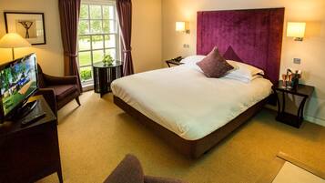A hotel room with a large bed, a TV, a desk, and a window with curtains.