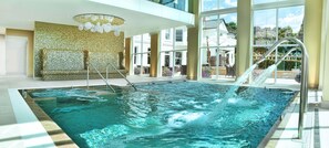 A large indoor swimming pool with clear water, a metal ladder, and a view of a house through large windows.