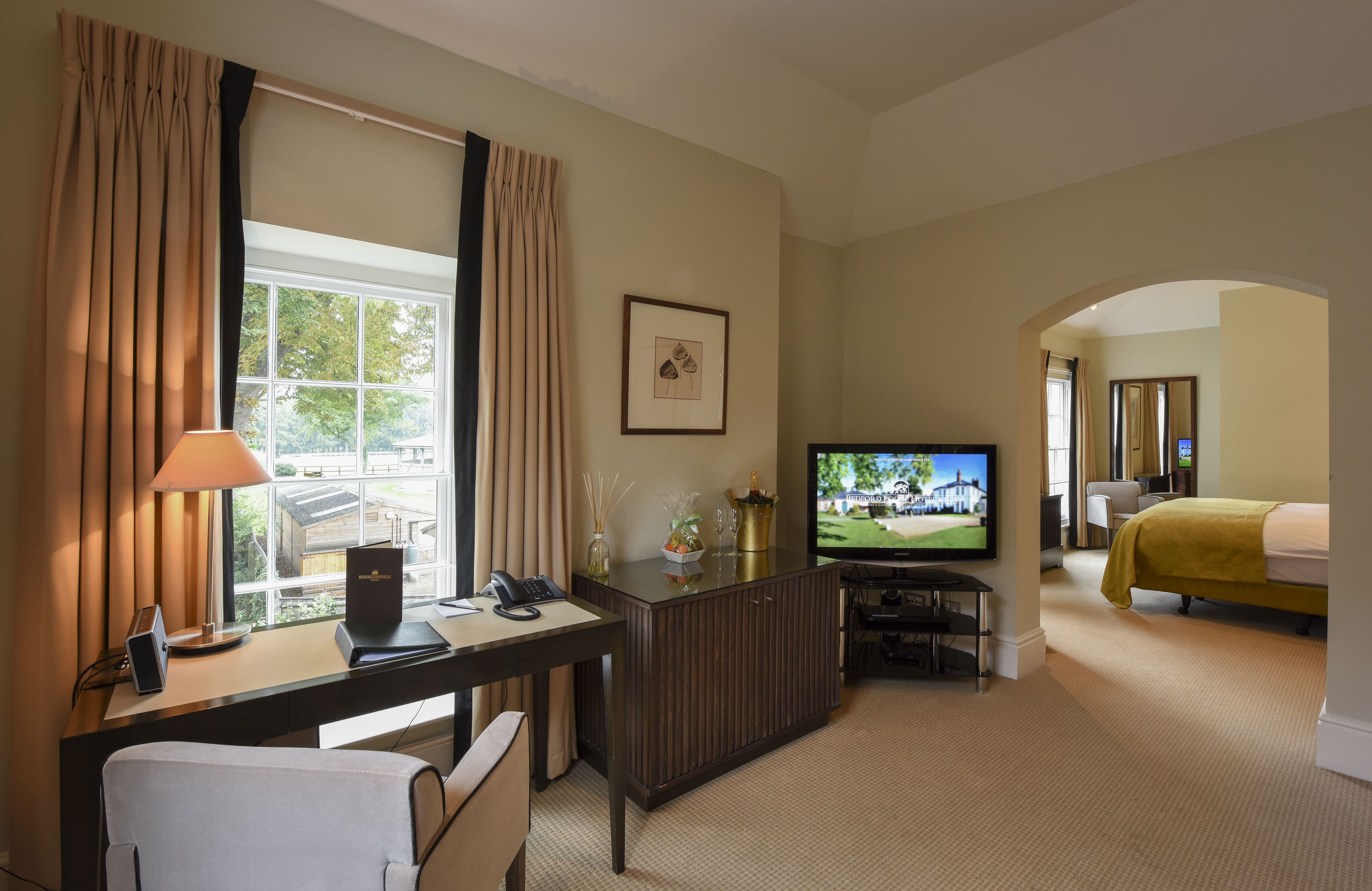 A hotel room with a desk, television, bed, and a view of a golf course.
