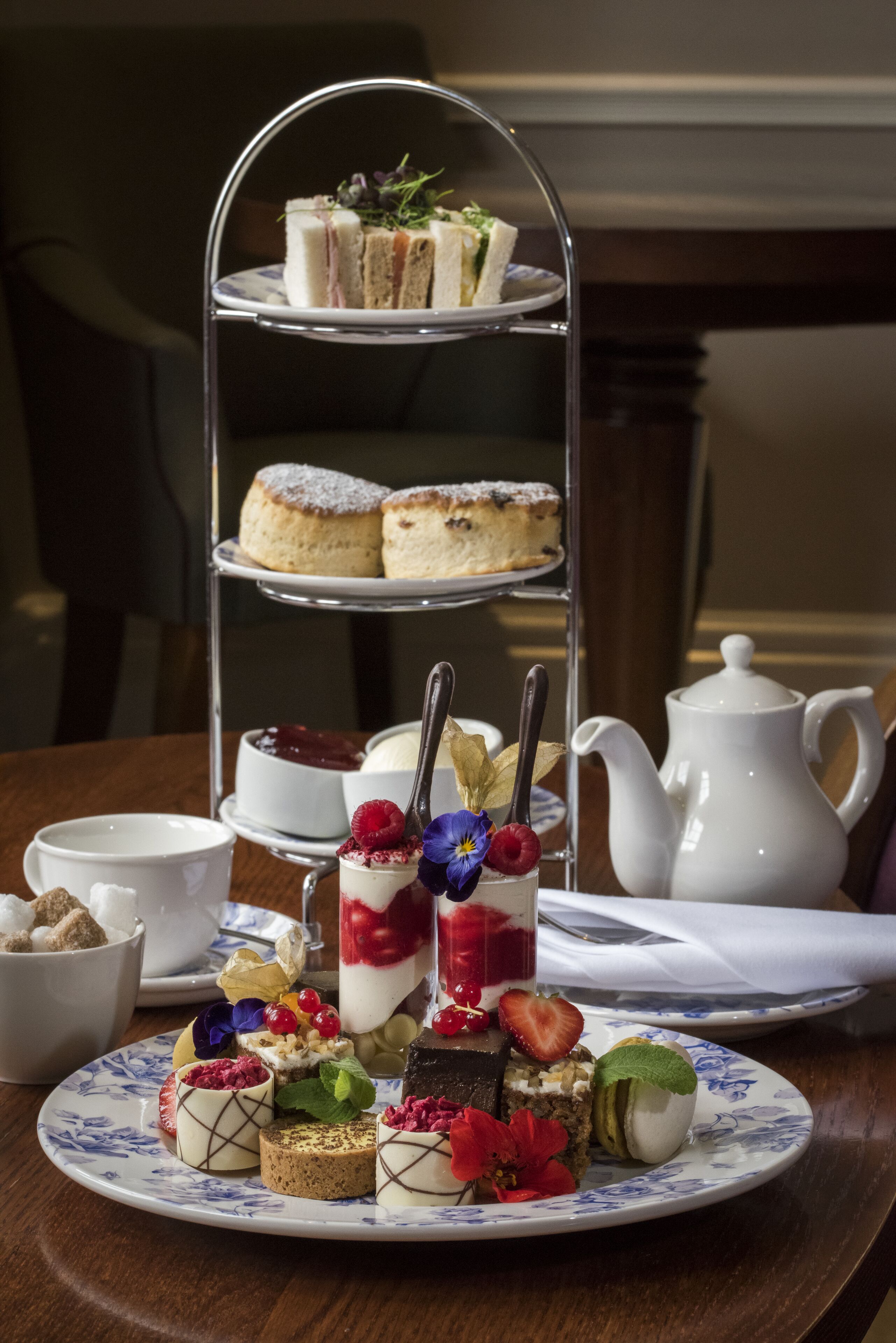 A tiered dessert stand with various pastries and a teapot on a table.