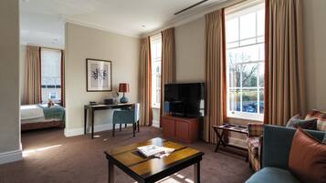 A hotel room with a bed, a desk with a chair, a television, a sofa, and a window with curtains.