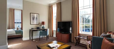 A hotel room with a bed, a desk with a chair, a television, a sofa, and a window with curtains.