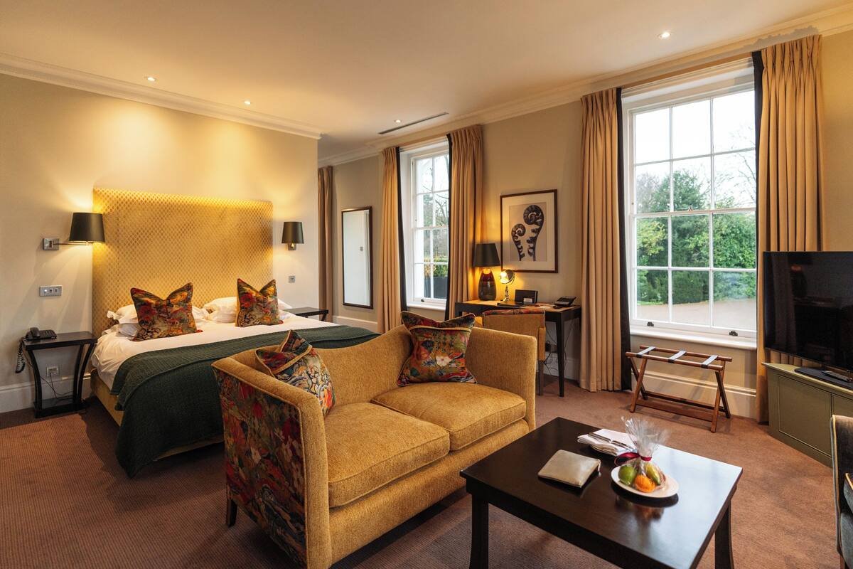 Een hotelkamer met een bed, een bank, een salontafel, een televisie en een raam met gordijnen.