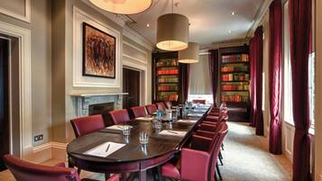 A formal meeting room with a long table, red chairs, and bookshelves filled with books.