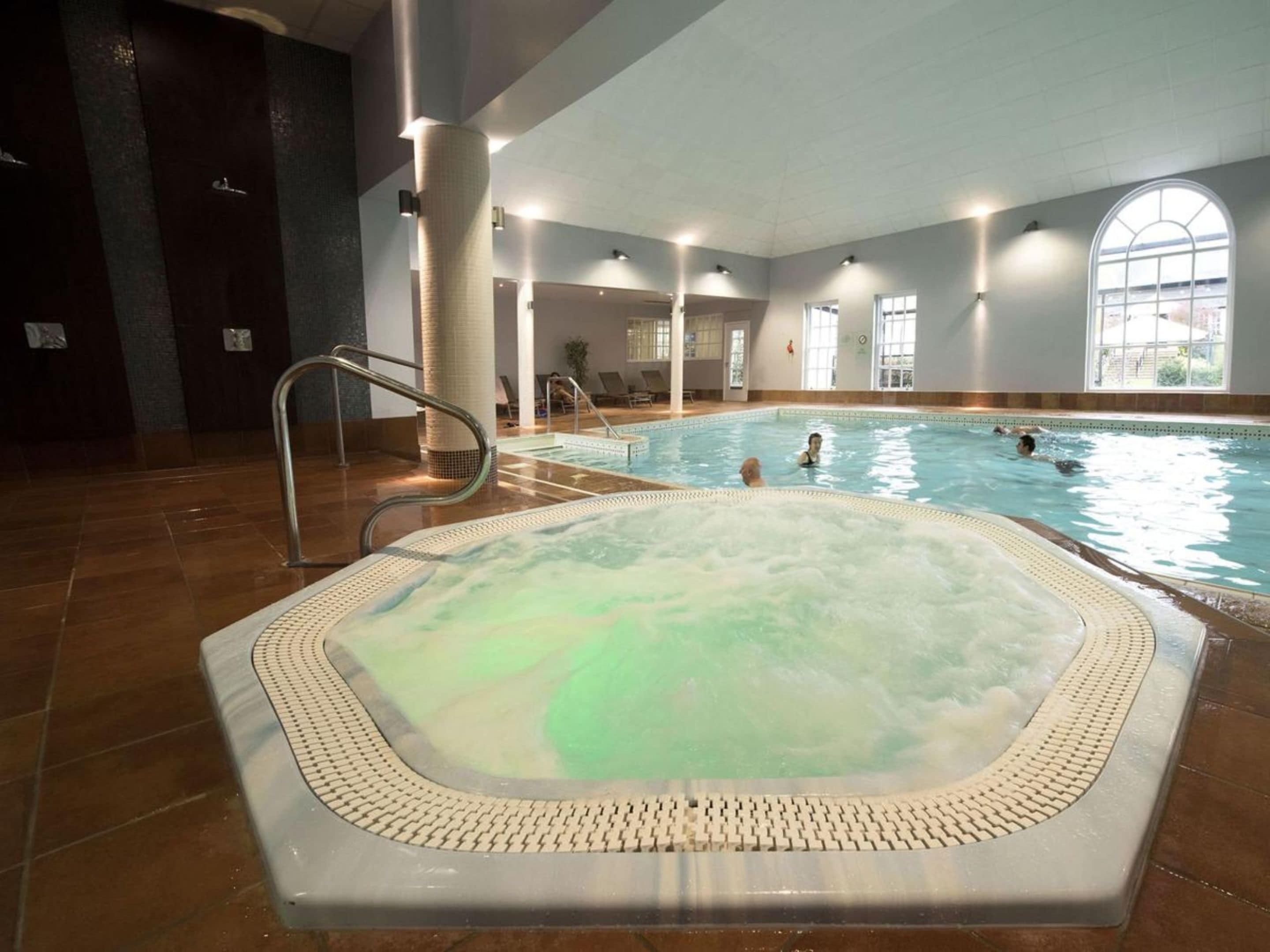 An indoor swimming pool with a hot tub, tiled flooring, and large windows.