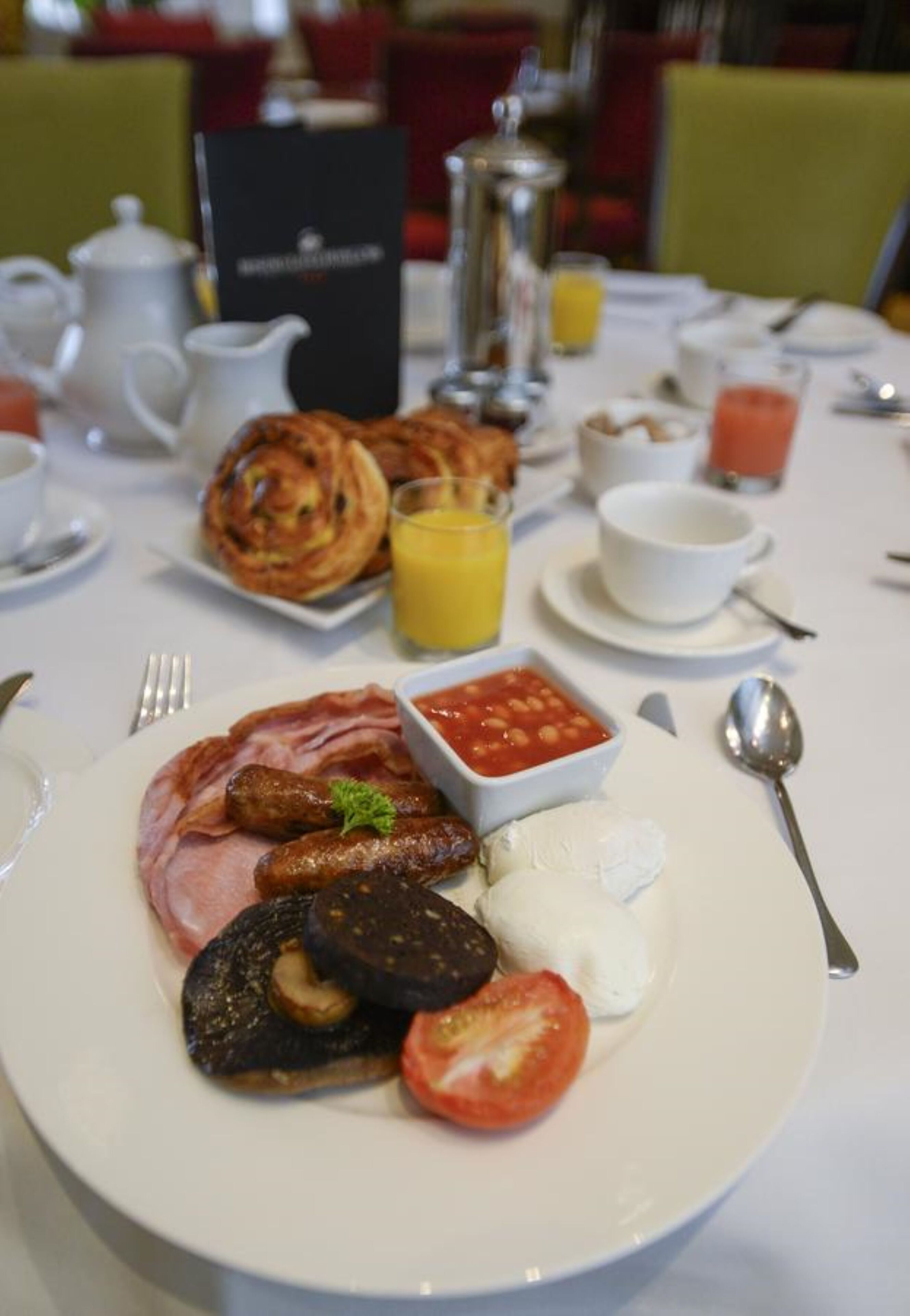 Une table de petit-déjeuner avec divers plats, notamment des œufs, des saucisses, des tomates et un bol de sauce.