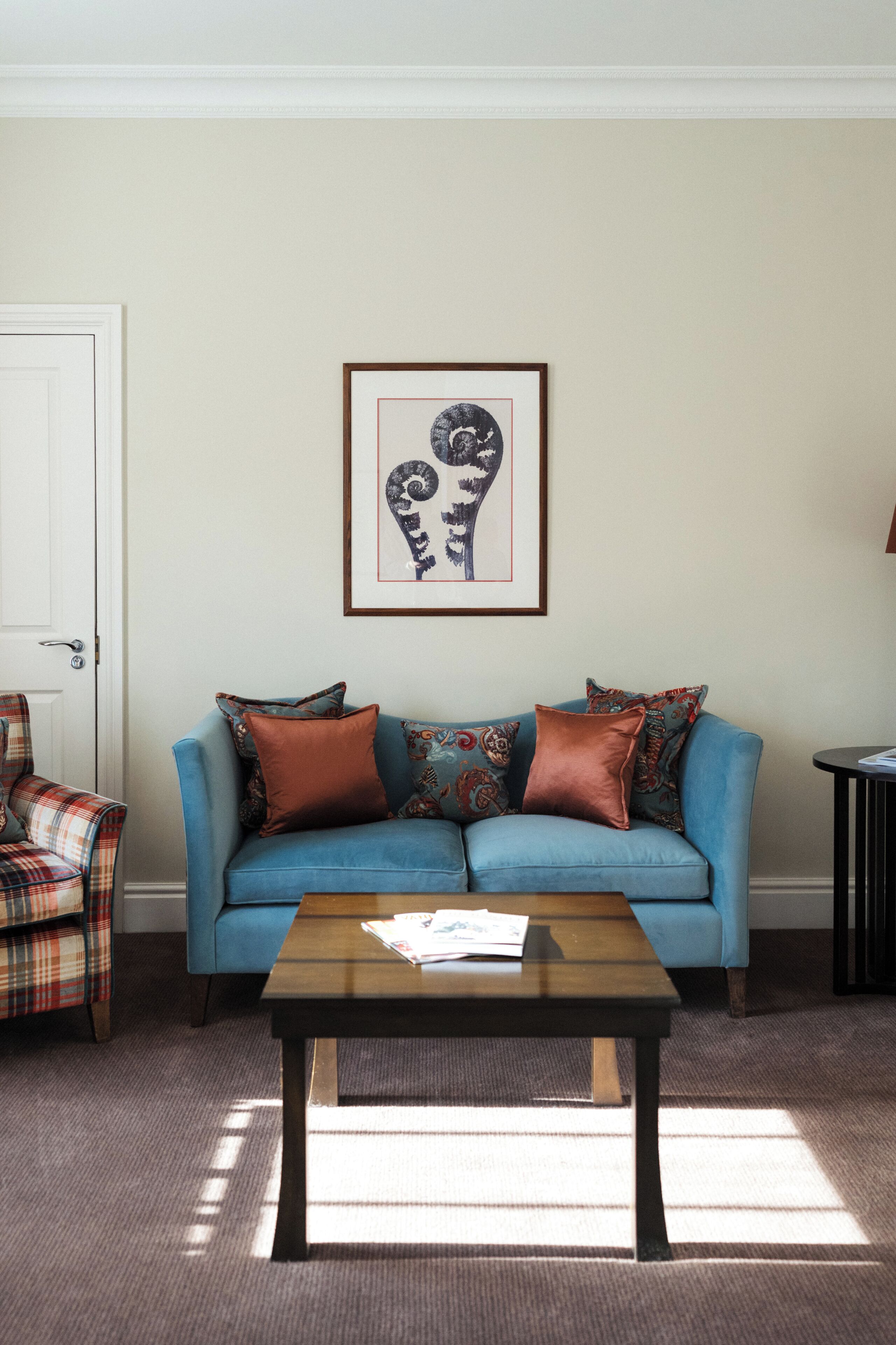 A living room with a blue sofa, a plaid armchair, a coffee table, and a framed artwork on the wall.