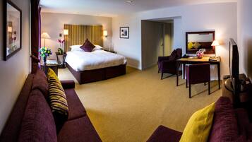 A hotel room with a large bed, a desk, a chair, and a sofa.
