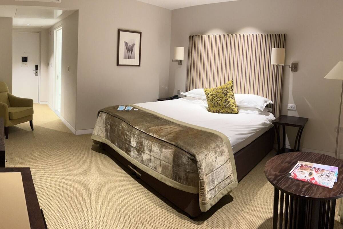 Een hotelkamer met een bed, een bureau met telefoon, een stoel, een spiegel en een nachtkastje met lamp.