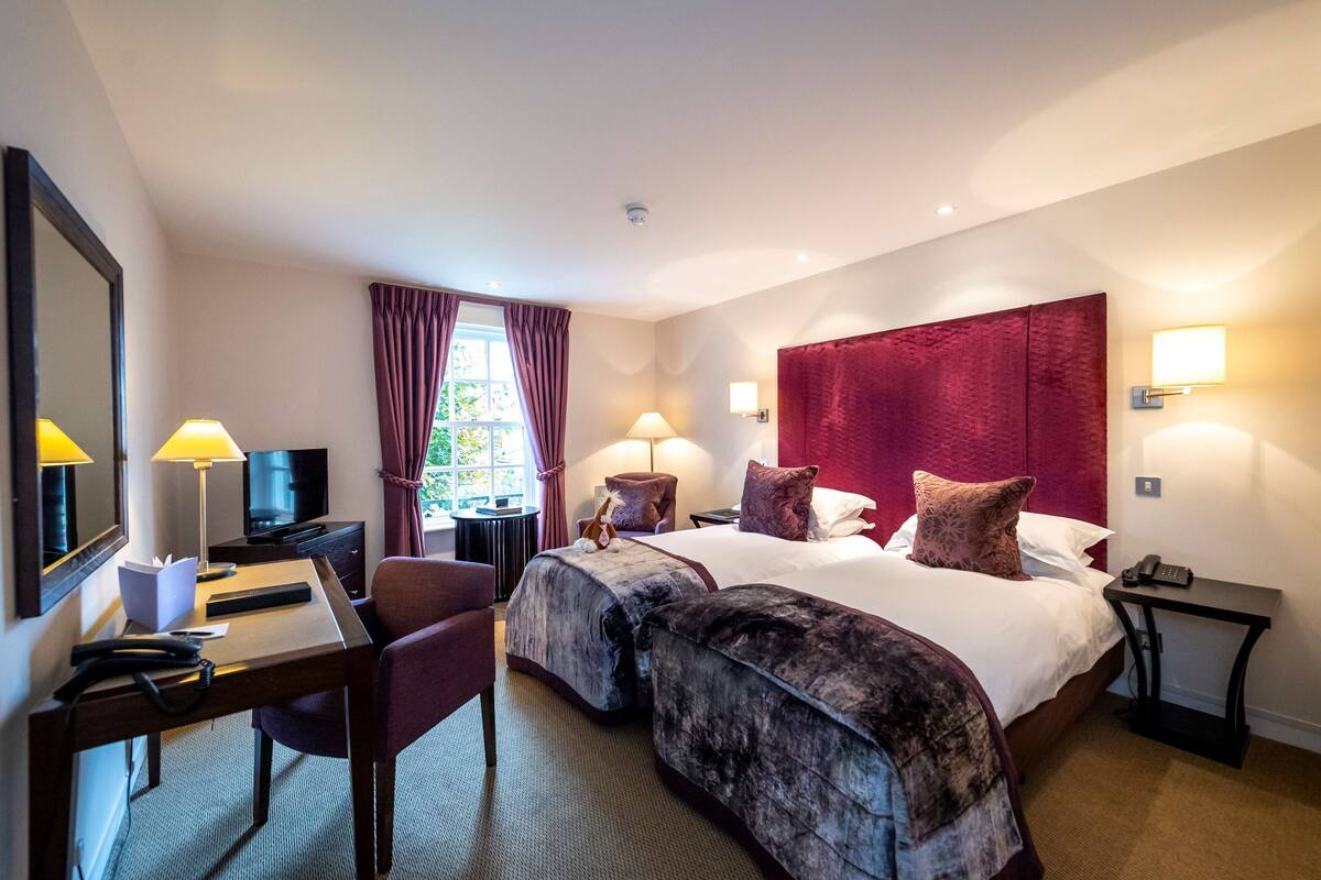 Een hotelkamer met een groot bed, twee nachtkastjes, een bureau met stoel, een televisie en een raam met gordijnen.