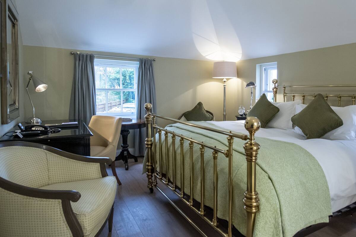 Een hotelkamer met een groot bed, een bureau met een lamp, een stoel en een raam met gordijnen.
