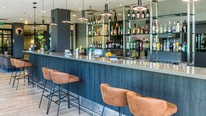 A modern bar area with a long counter, multiple bar stools, and a variety of liquor bottles.