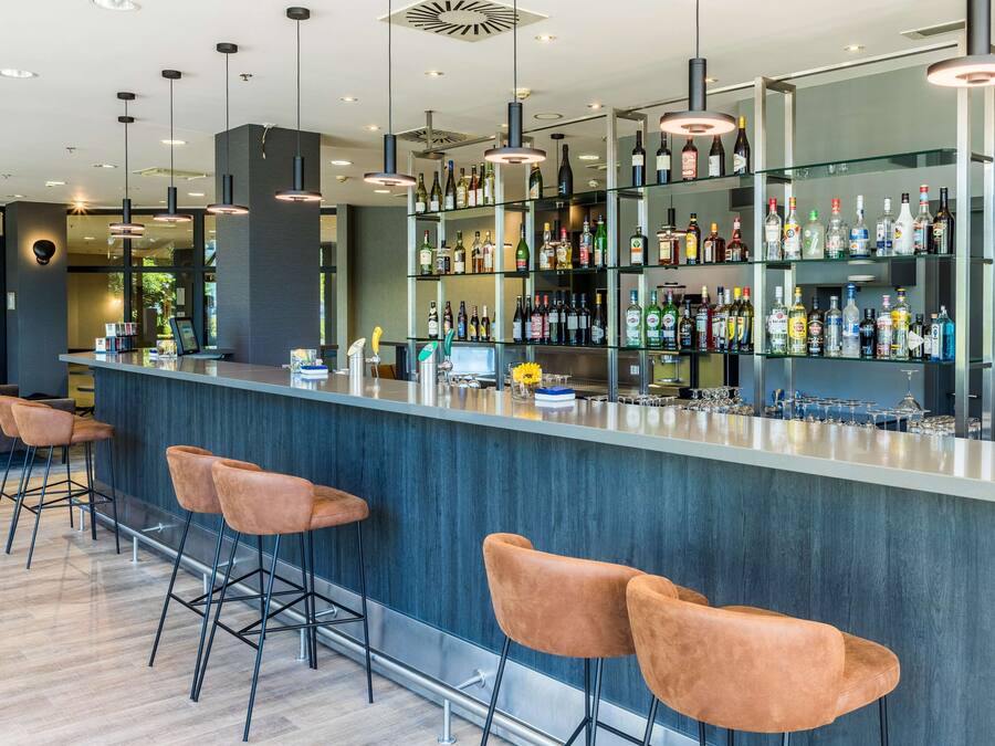 A modern bar area with a long counter, multiple bar stools, and a variety of liquor bottles.