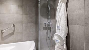 Un baño moderno con ducha envuelta en vidrio, una bañera blanca y un perchero con una toalla colgada.