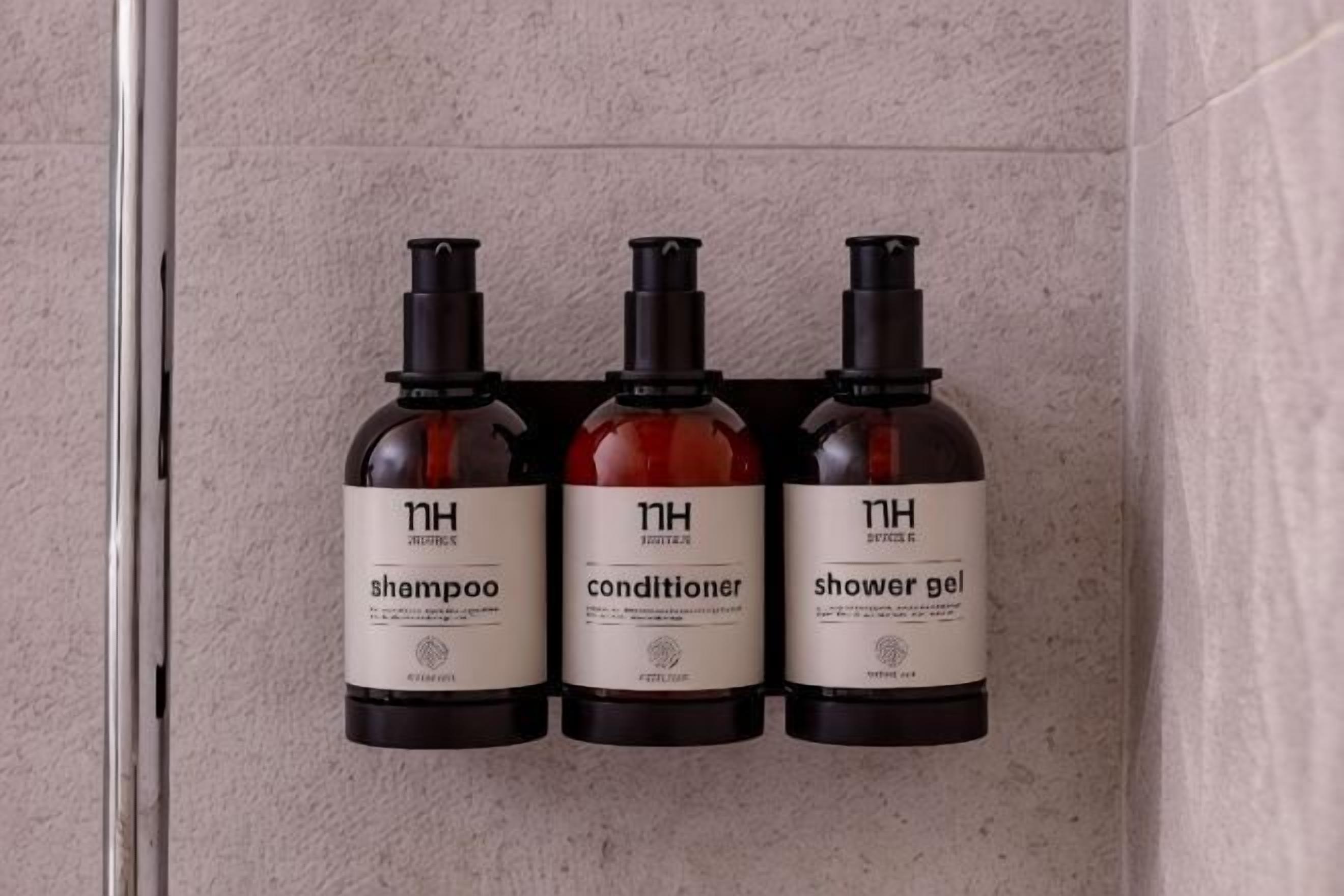 Three bottles of shampoo, conditioner, and shower gel on a wall.