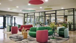 A modern lobby with green and red sofas, a marble floor, and large windows.