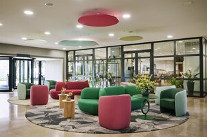 A modern lobby with green and red sofas, a marble floor, and large windows.