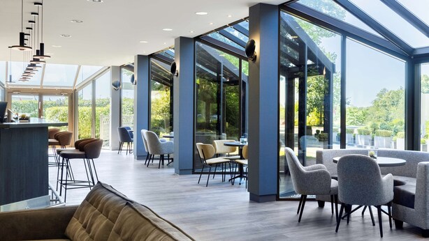 A spacious indoor area with a high ceiling, large windows, and modern furniture.