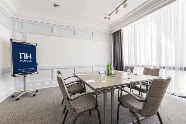 A conference room with a large table, four chairs, a projector screen, and a window with curtains.
