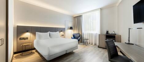 A hotel room with a bed, a desk, a chair, a small table, and a TV.