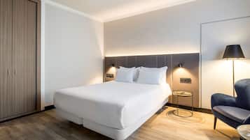A hotel room with a large bed, a wardrobe, a bedside table with a lamp, and a chair.