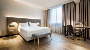 A modern hotel room with a large bed, bedside tables, a desk, and a chair.