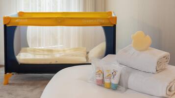 Uma cama com berço amarelo e azul, uma toalha enrolada e uma mamadeira.