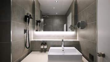 A modern bathroom with a rectangular sink, a handheld hair dryer, and two bottles of shampoo and conditioner on the countertop.