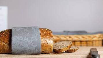 A loaf of bread with a patterned cloth on it, sliced bread, and a knife on a wooden surface.