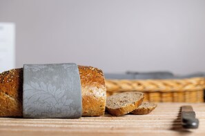 A loaf of bread with a patterned cloth on it, sliced bread, and a knife on a wooden surface. - Dombås Hotel (Dovre)