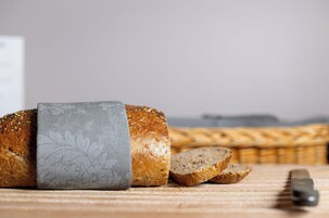 Una hogaza de pan sobre un paño estampado, rebanadas de pan y un cuchillo sobre una superficie de madera.