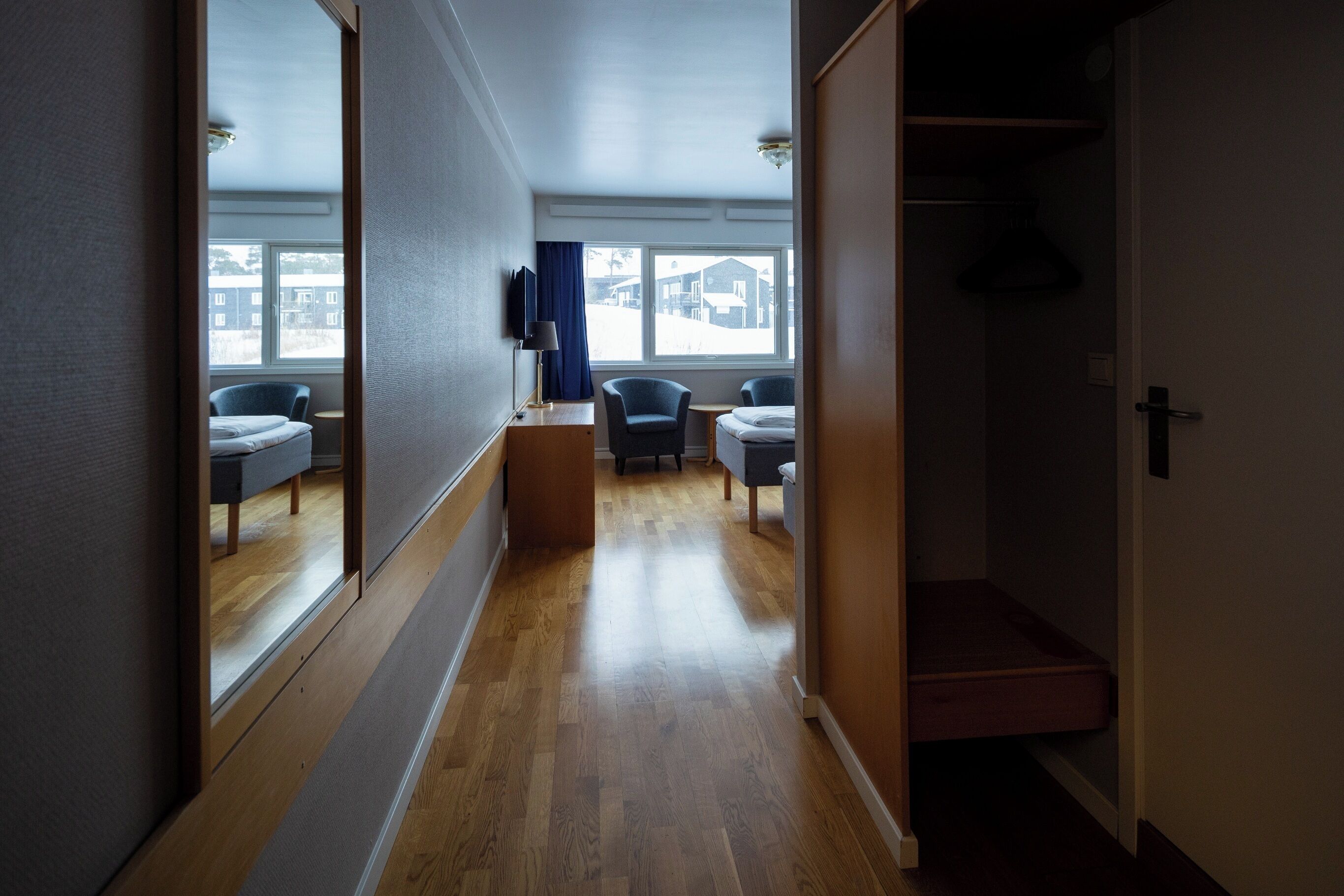 A hallway with a wooden floor, a mirror, a TV, and a window with a view of houses.
