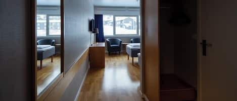 A hallway with a wooden floor, a mirror, a TV, and a window with a view of houses.