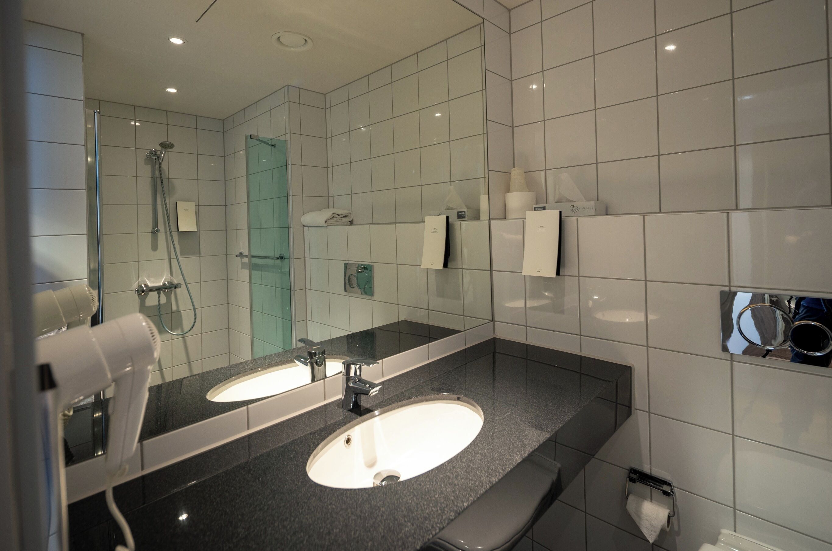 A modern bathroom with two sinks, a glass shower enclosure, and a mirror with a towel rack.
