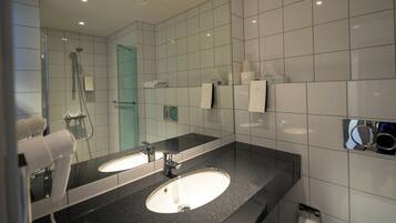 Un baño moderno con dos lavamanos, cabina de ducha con mampara de cristal y espejo con toallero.